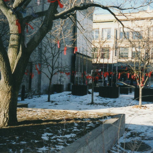 Au Parc de l’Espoir, le soir du 1er décembre 2004, quatre personnes portent des masques d’un visage dessiné. Chacune tient une pancarte accompagnée d’un mot (exclusion, injustice, stigmatisation, mot non-visible. Crédit photo : René Leboeuf. Fonds Michael Hendricks-René Leboeuf. Collection des Archives gaies du Québec.
